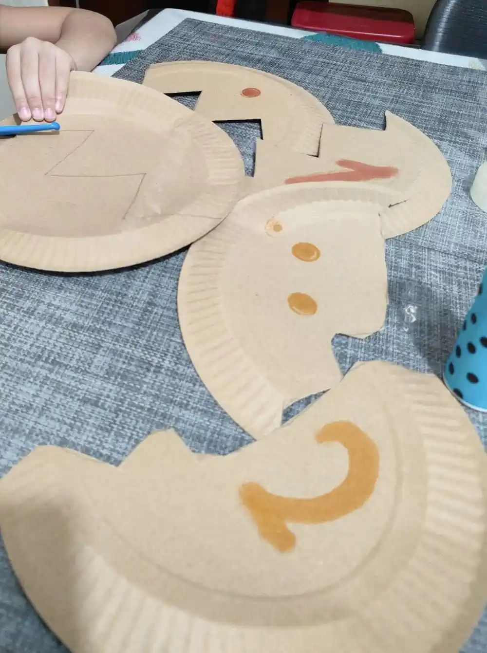 Paper plates cut into pieces with numbers and dots drawn on them, and a child hand holding a plate while cutting